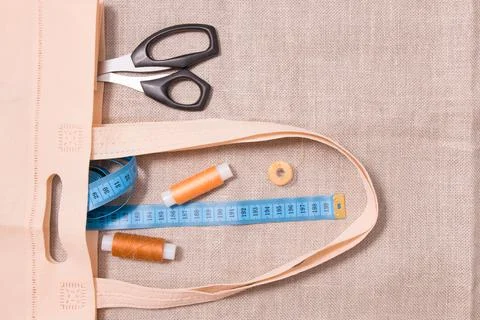 Scissors, measuring tape and several spools of thread in an eco bag on linen  Stock Photos