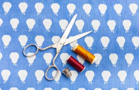Scissors, a needle and two spools of red and yellow thread together with a Stock Photos