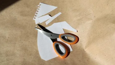 Scissors with an orange handle lying on a cut white paper against a brown k.. Stock Photos