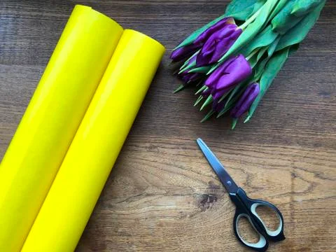 Scissors, packaging paper and violet tulips on wooden table. Cutting bouquet, ma Stock Photos