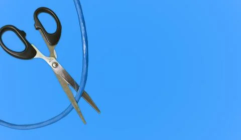 Scissors Severing a Blue Cable Against a Vibrant Blue Backdrop: Symbolizing.. Stock Photos