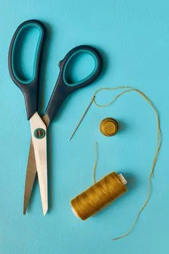 Scissors, spool of thread, needle and thimble on cyan background, flat lay Stock Photos