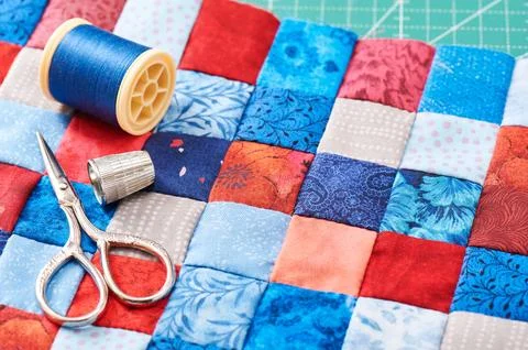 Scissors, thread and thimble lying on blue and red square pieces of fabric .. 스톡 사진