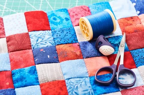 Scissors, thread and thimble lying on blue and red square pieces of fabric .. Stock-Fotos