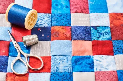 Scissors, thread and thimble lying on blue and red square pieces of fabric .. Stock Photos