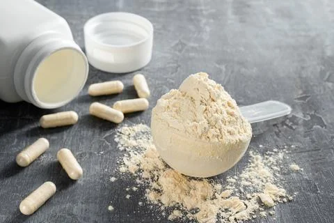 Scoop of whey or soy protein isolate, white capsules of bcaa, beta-alanine  Stock Photos
