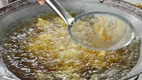 Scooping crispy fried food bits from hot boiling oil with a strainer. Stock Footage 342696439