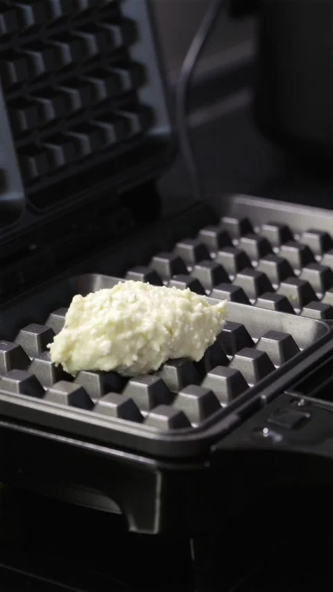 Scooping curd dough mixture into hot electric waffle maker machine Stock Footage 336902543