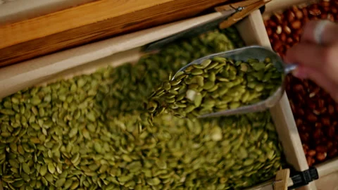 Scooping pumpkin seeds from bulk bin in organic grocery store. Close-up of Stock Footage 291587463