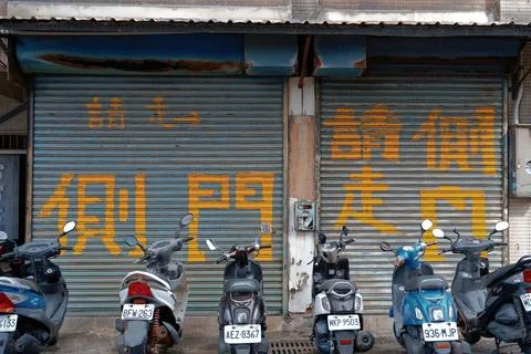 Scooters Parked by Rusty Shutter with Hand-Painted Chinese Text Taiwan Stock-Fotos