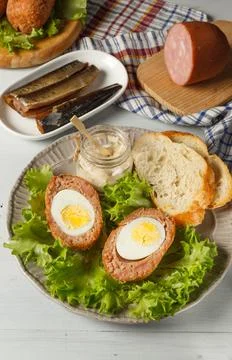 Scottish-style eggs cut in half on a plate with lettuce leaves, baguette slices Stock Photos