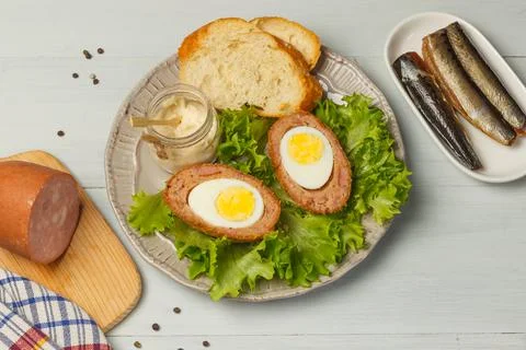 Scottish-style eggs cut in half on a plate with lettuce leaves, baguette slices Stock Photos
