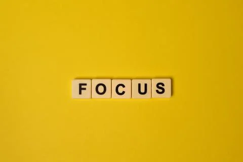 Scrabble letters with text FOCUS isolated on a yellow background Foto stock