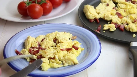 Scrambled eggs and bacon bits eaten with fork and knife from a blue plate Stock Footage 74165335
