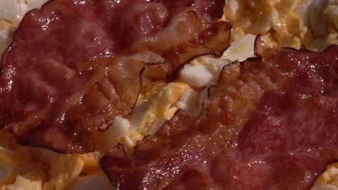 Scrambled eggs and sliced crispy wavy bacon, rotating close up. Stock Footage 99850922