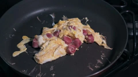 Scrambled eggs and sliced hot dogs cooking in a dark skillet Stock-Footage 329627570