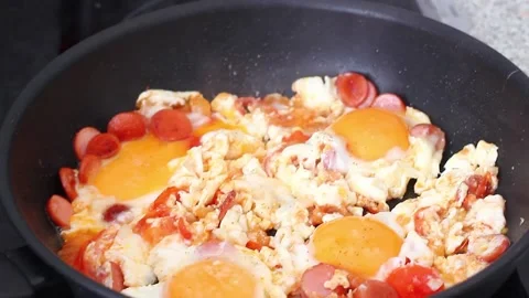 Scrambled eggs are fried with slices of sausage and chopped tomatoes for Stock Footage 156640839
