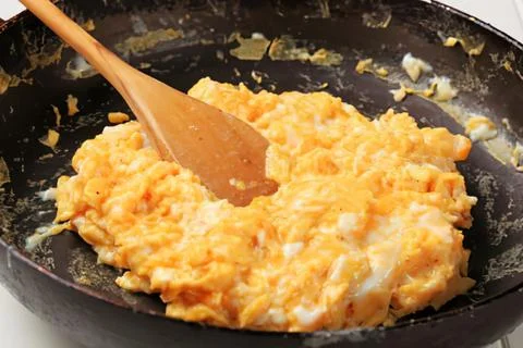 Scrambled eggs being cooked in a black pan Stock Photos