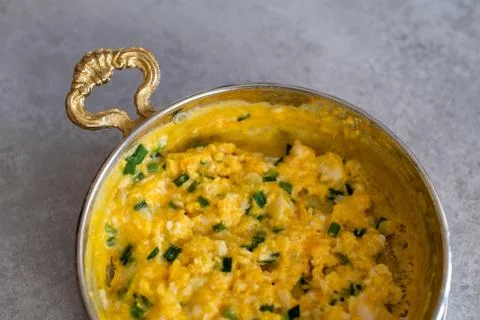 Scrambled eggs with cheese and spring onion. Served in a copper pan. Stock Photos