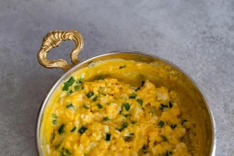 Scrambled eggs with cheese and spring onion. Served in a copper pan. Stock Photos