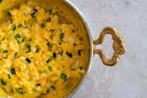 Scrambled eggs with cheese and spring onion. Served in a copper pan. Stock Photos