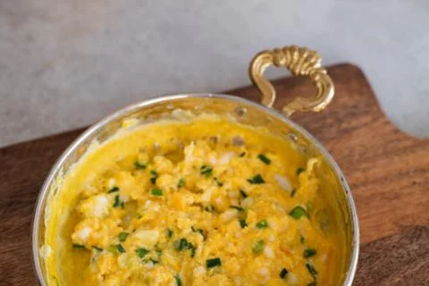 Scrambled eggs with cheese and spring onion. Served in a copper pan. Stock Photos