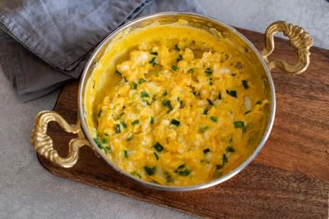 Scrambled eggs with cheese and spring onion. Served in a copper pan. Stock Photos