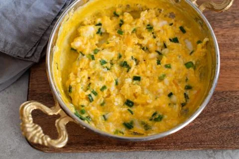 Scrambled eggs with cheese and spring onion. Served in a copper pan. Stock Photos