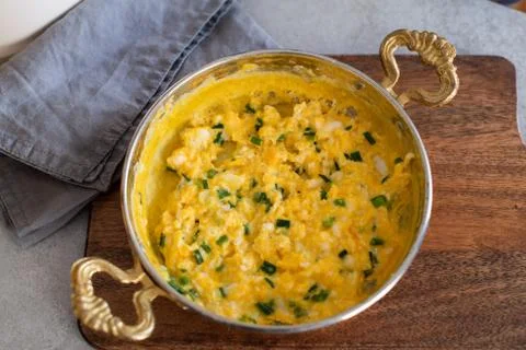 Scrambled eggs with cheese and spring onion. Served in a copper pan. Stock Photos
