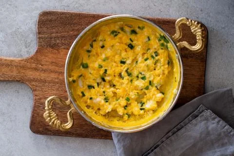 Scrambled eggs with cheese and spring onion. Served in a copper pan. Stock Photos