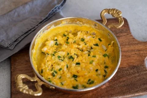Scrambled eggs with cheese and spring onion. Served in a copper pan. Stock Photos
