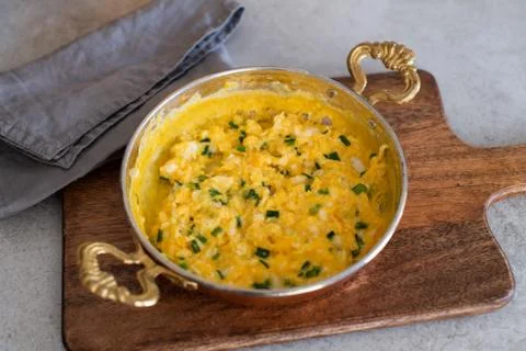 Scrambled eggs with cheese and spring onion. Served in a copper pan. Stock Photos