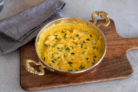 Scrambled eggs with cheese and spring onion. Served in a copper pan. Stock Photos
