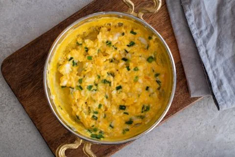 Scrambled eggs with cheese and spring onion. Served in a copper pan. Stock Photos