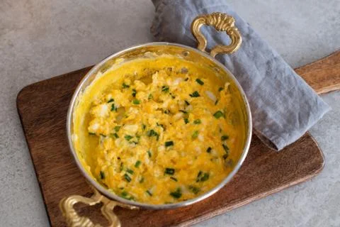 Scrambled eggs with cheese and spring onion. Served in a copper pan. Stock Photos