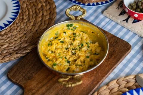 Scrambled eggs with cheese and spring onion. Served in a copper pan. Stock Photos