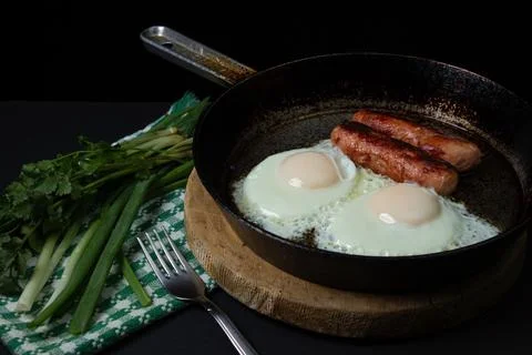 Scrambled eggs on a dark background. Fried eggs with fried sausages. Stock Photos