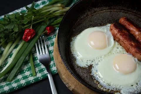 Scrambled eggs on a dark background. Fried eggs with fried sausages. Stock Photos