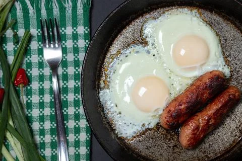 Scrambled eggs on a dark background. Fried eggs with fried sausages. Stock Photos
