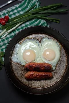 Scrambled eggs on a dark background. Fried eggs with fried sausages. Stock Photos