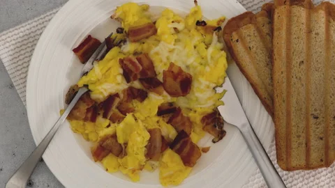 Scrambled eggs fried with cheese, and served with fried bacon and toasted breade Stock Footage 225856018