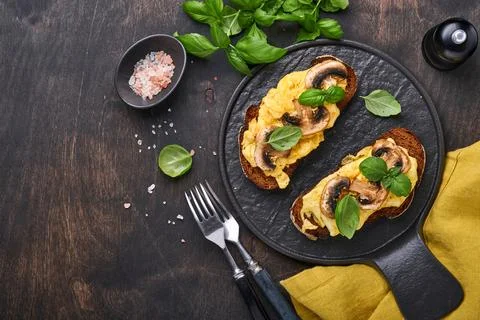 Scrambled eggs with fried mushrooms and basil on bread on black table backgro Stock Photos