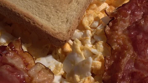 Scrambled eggs, slice of bread and fried crispy bacon, fading rotating to stop Video stock 99851040