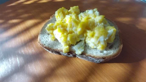 Scrambled eggs on a slice of fresh rye bread on a wooden table Stock Footage 333643886