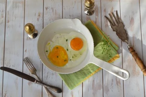Scrambled eggs in a small white pan on a white shabby background flat lay Stock Photos