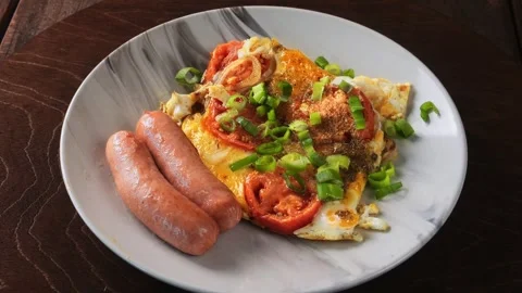 Scrambled eggs with tomatoes, cheese and fried sausages sprinkled with green Stock Footage 288241417