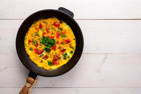 Scrambled eggs with tomatoes in an old cast iron pan on a white wooden backgr Stock Photos