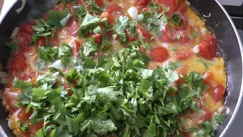 Scrambled eggs with vegetables and herbs are cooked in a pan Stock Footage 164189531