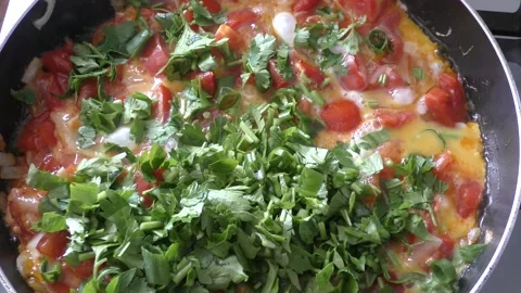 Scrambled eggs with vegetables and herbs are cooked in a pan Stock Footage 164189647