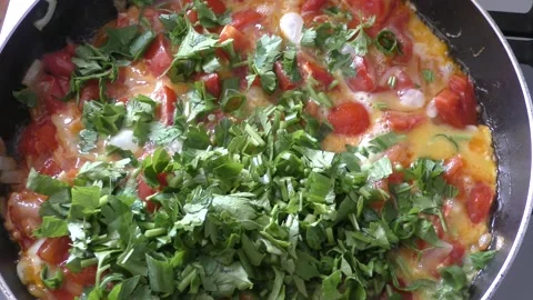 Scrambled eggs with vegetables and herbs are cooked in a pan Stock Footage 164189784